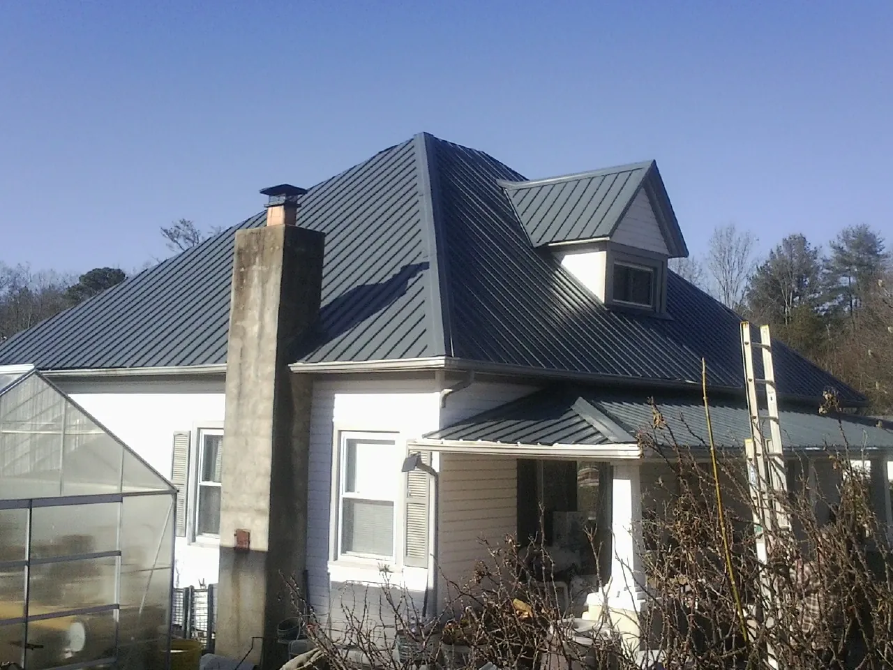 Dark blue standing seam metal roof on a white farmhouse with dormer — Slate & Tile Roof Repair by Roofing Brothers in Santa Claus