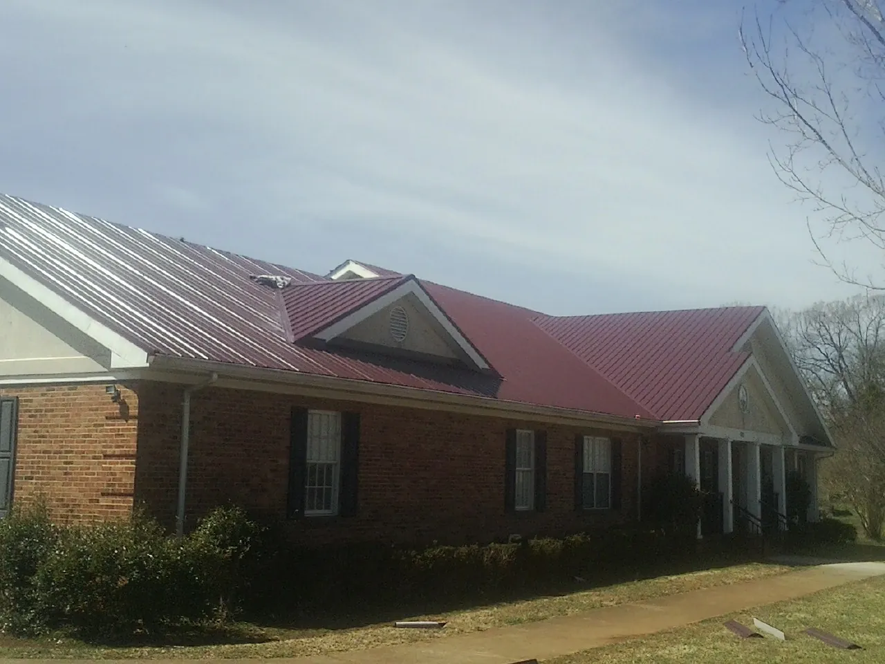Red metal roof with gabled entries on a long brick building, from a Hail Damage Roof Repair job in Santa Claus