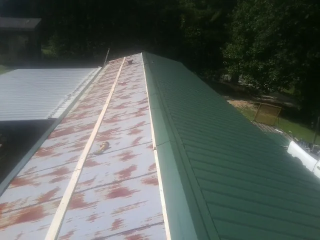 Old rusted panels beside newly installed green metal roofing — Wind Damage Roof Repair by Roofing Brothers in Santa Claus