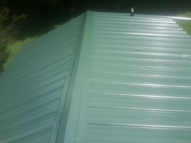 New green metal panels meeting at the ridge of a roof — Flat Roof Repair work by our crew in Santa Claus