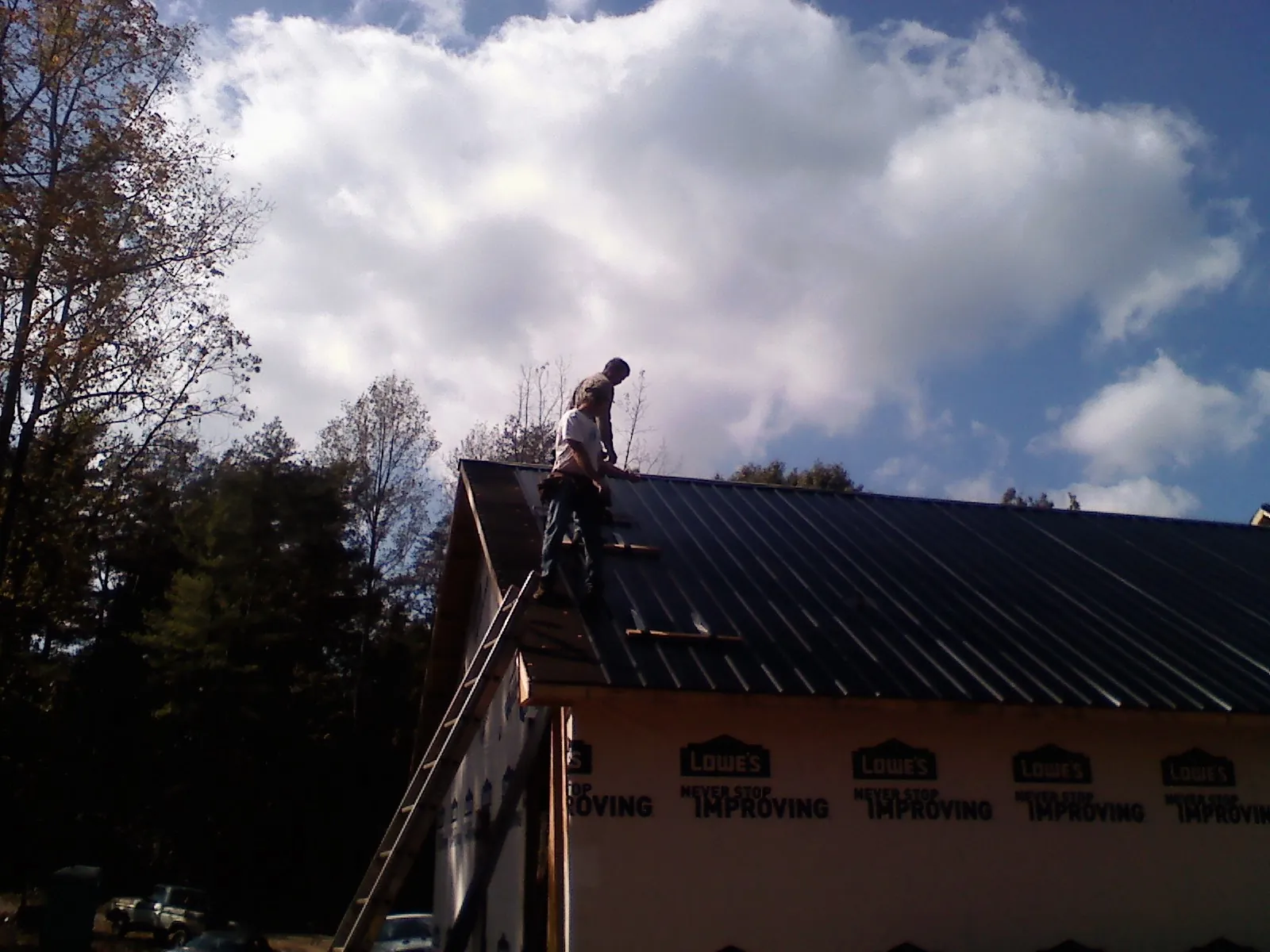 Roofer fastening dark metal panels high against a cloudy sky, from a Roof Inspection job in Santa Claus