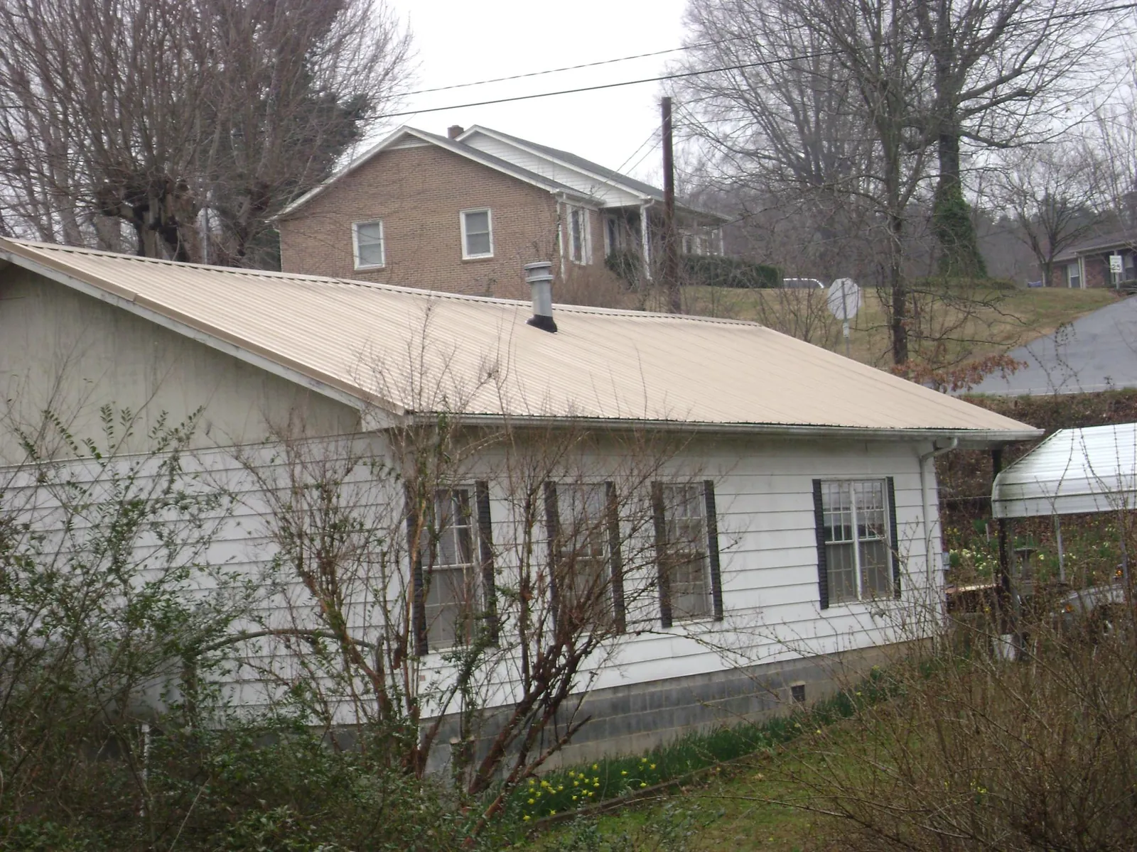 Tan metal roof on a white sided house set into a hillside — Commercial Roofing by Roofing Brothers in Santa Claus