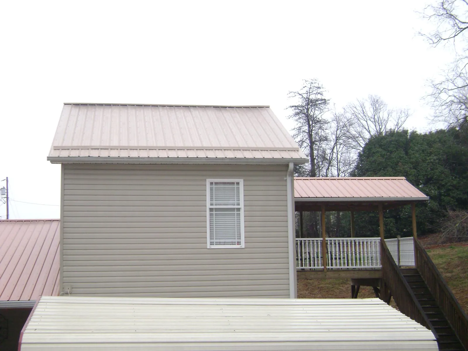 Tan metal roofs on a two story addition and attached porch, from a Roof Replacement job in Santa Claus
